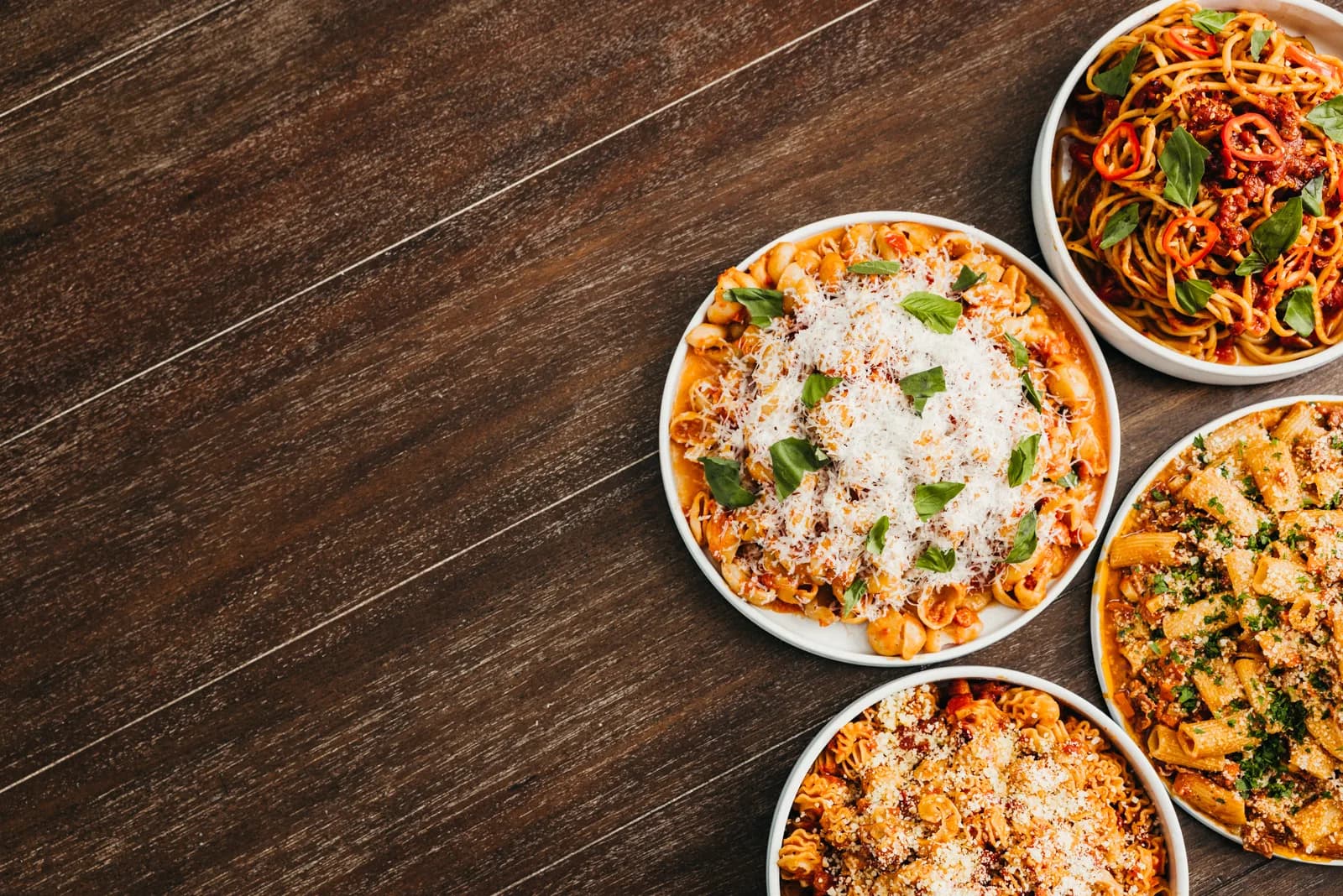 Bowls of pasta laid out on a dark wooden board, photographed from above