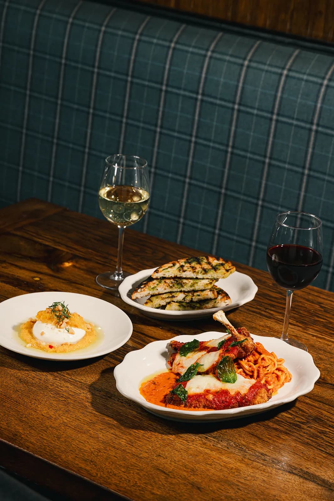 Two plates and glasses of wine in a teal banquette booth