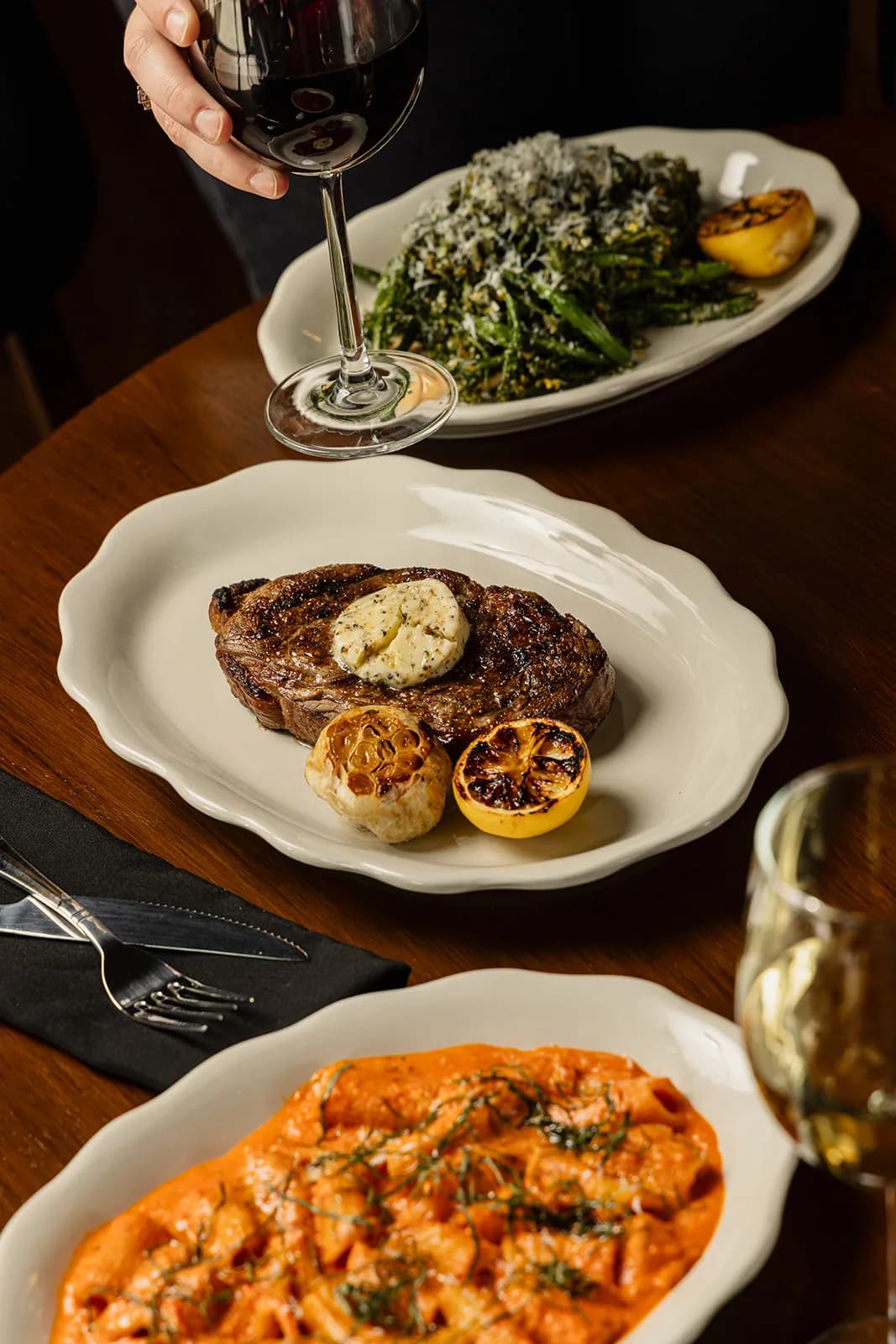 A spread across the table at Losanti – Columbus: steak, greens and pasta with wine poured