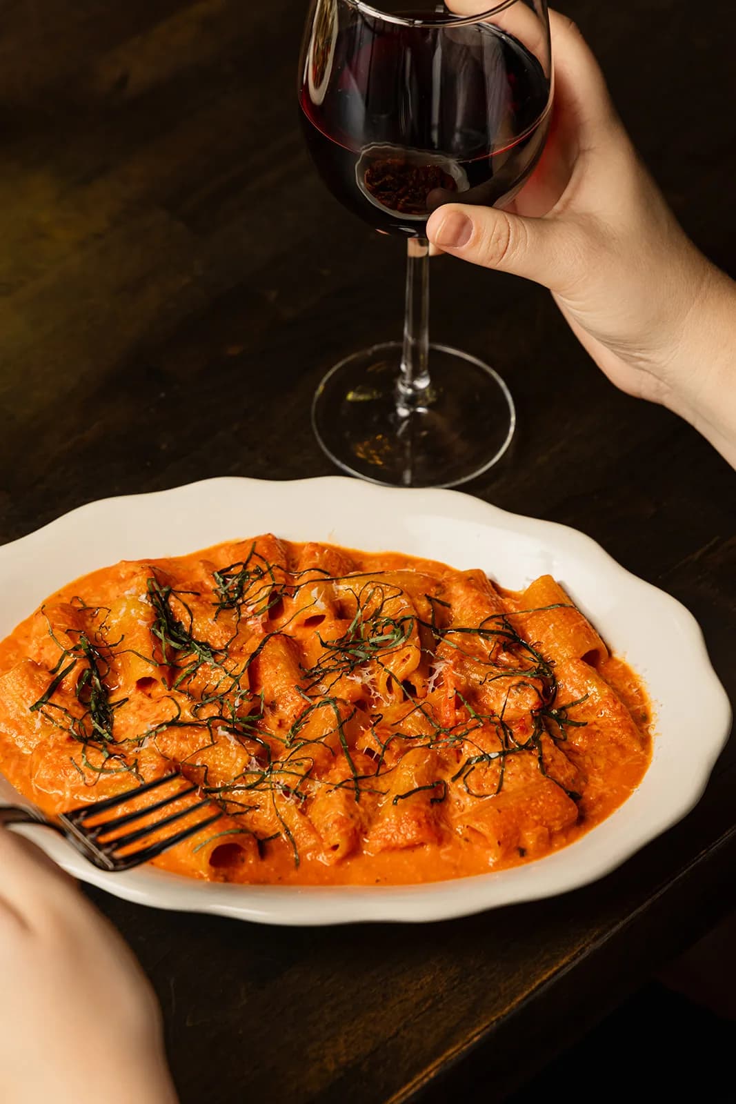 A bowl of pasta on the table beside a glass of red wine