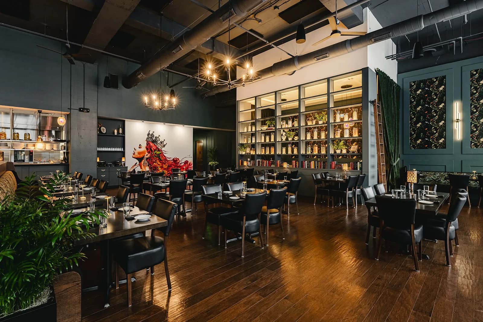 The dining room at Marigold under industrial ductwork, with a wall of lit shelving and a red floral arrangement at the back